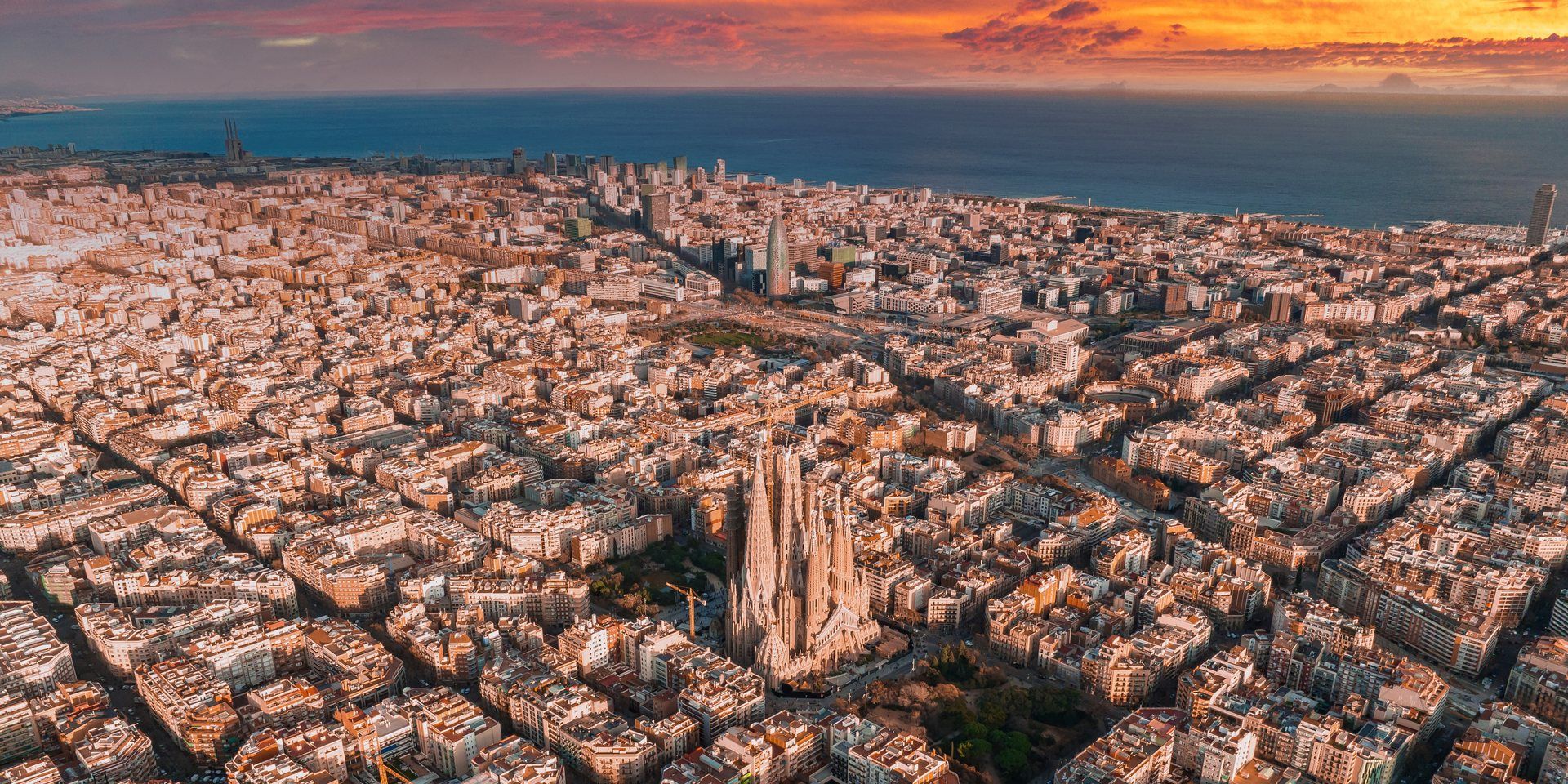 Aerial view of Barcelona at sunset, the Sagrada Família at the centre, the Mediterranean and a blazing sky on the horizon.
