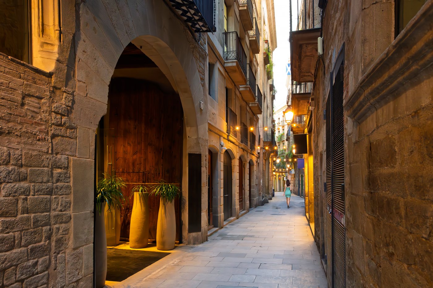 A cobbled alley in Barcelona's Gothic quarter at nightfall, lit by warm lanterns.