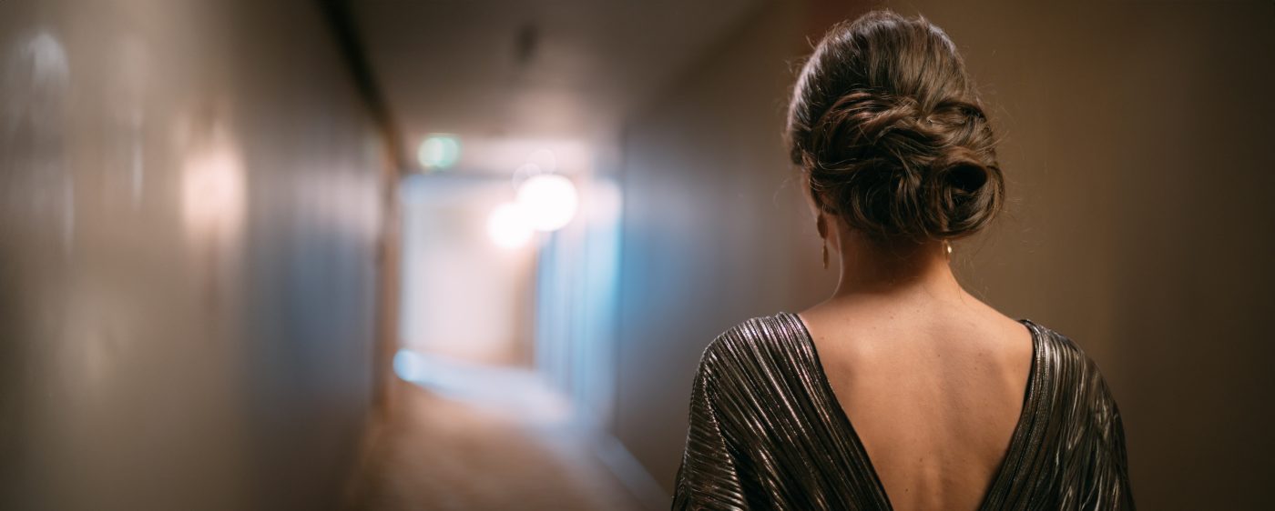 Elegant woman in an evening dress seen from behind, walking down a hotel corridor