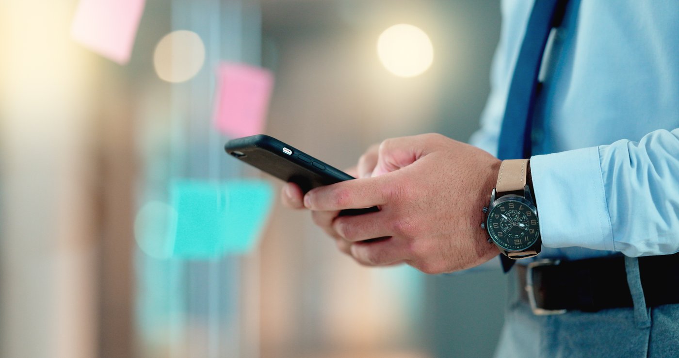 A well-dressed man composing a message on his phone, a watch on his wrist.